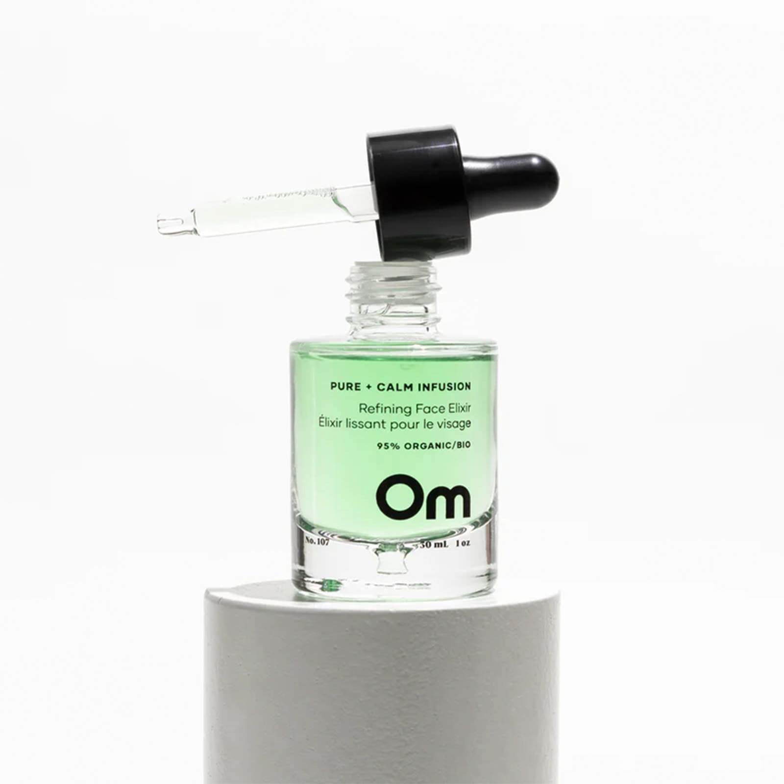 Product shot of Om Organics Pure + Calm Infusion Refining Face Elixir glass bottle on pedestal